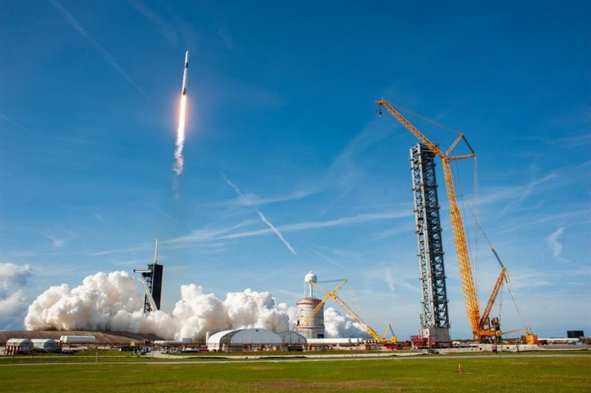 On a sunny day, a Falcon 9 rocket lifts off from a launch pad.