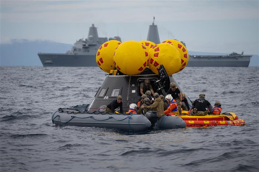 Deux bateaux pneumatiques transportant des gens flottent devant une maquette de vaisseau spatial.