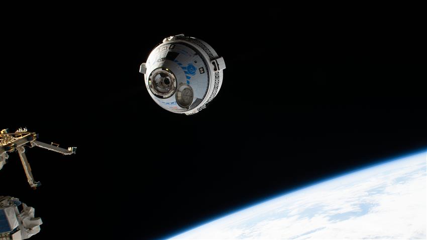 Un vaisseau spatial Starliner s'approche de la Station spatiale internationale. On voit une partie de la Terre.
