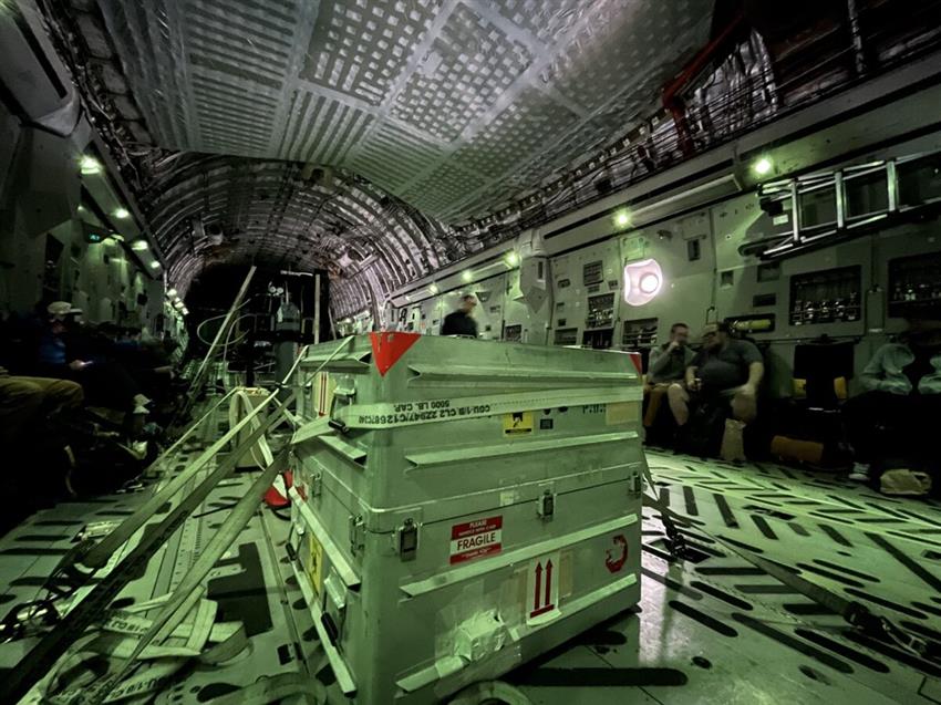 A shipping container is strapped in a cargo plane with a few people sitting along the fuselage.